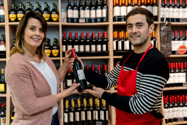 istock Female customer and friendly salesman at the wine section holding a bottle together while facing camera smiling 1172975621