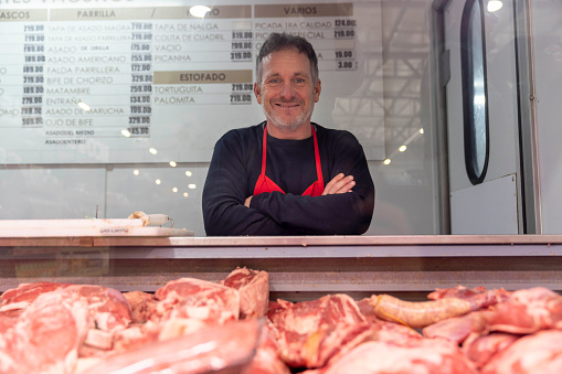 Portrait of latin american butcher leaning on counter smiling at camera very happy