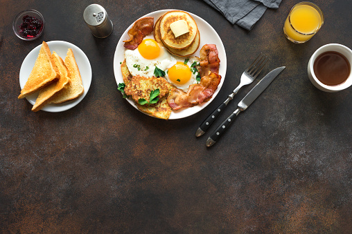 Full American Breakfast on white, top view, copy space. Sunny side fried eggs, roasted bacon, hash brown, pancakes, orange juice and coffee for breakfast.