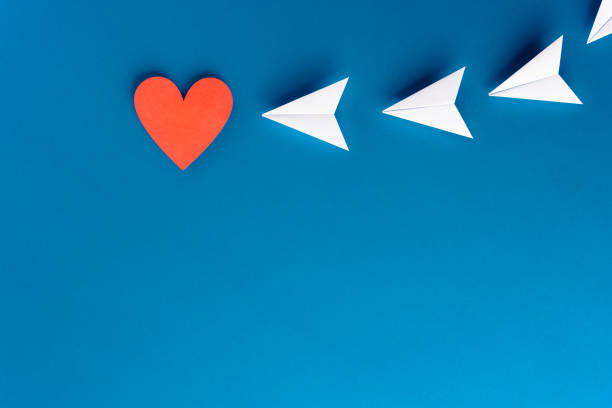 Focus, assertiveness, work yourself concept. Paper heart shape with airplane on blue background stock photo