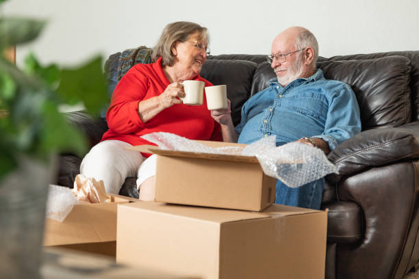 Tired Senior Adult Couple Resting on Couch with Cups of Coffee Surrounded with Moving Boxes stock photo