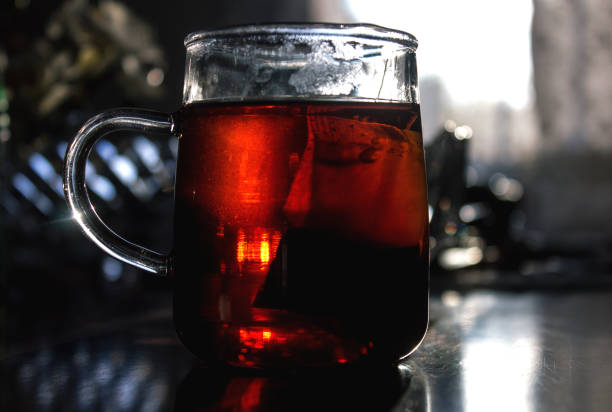 A teabag rests in a glass tea cup on wooden table in the morning,  in low angle close up  selective focus image with copy space.