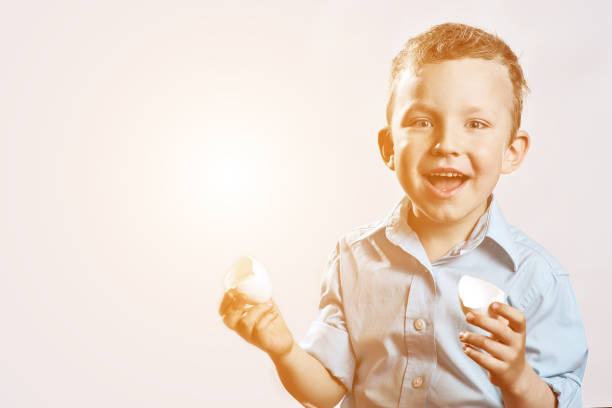 istock boy in a light shirt holding a shell from the egg and smiling on a light background 1173010925