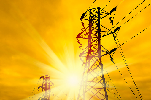 close up electricity power line tower over orange color sunset sky with shining sun