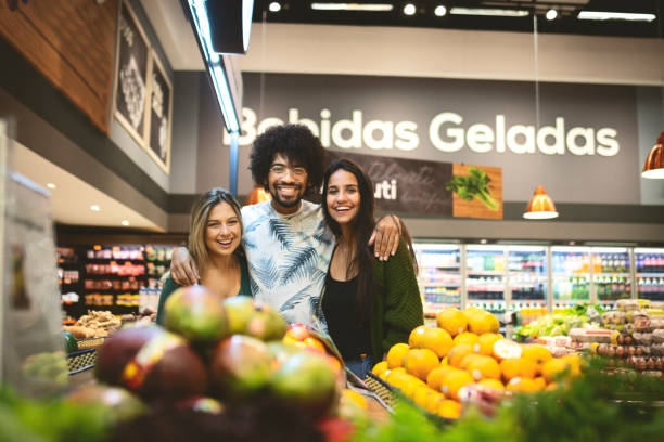 Group of friends shopping in a grocery and looking at camera Group of friends together in the supermarket reduction looking at camera finance business stock pictures, royalty-free photos & images