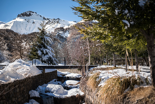 Winter landscape in Nevados de Chillán, during a sunny morning, with a river, a footbridge, snow and a mountain. August 07, 2019.