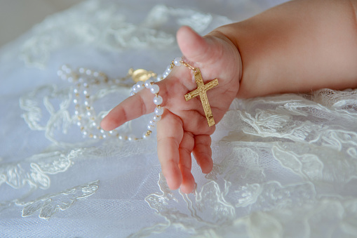 Child's hand with a crucifix on a white cloth.