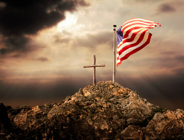 American flag at flagpole and wooden cross Conceptual image of waving American flag at flagpole and wooden cross over sunset sky cross shape cross religion christianity stock pictures, royalty-free photos & images