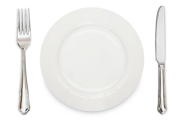 A white plate, knife and fork against a white background stock photo