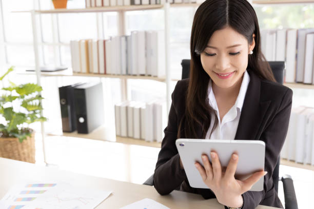 istock Happy Attractive businesswoman in black suit using a digital tablet while sit in desk at office building with natural light. Business and technology 1173046698