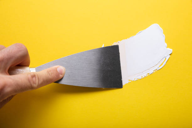 Painter Puttied Yellow Wall With Paint Trowel Close-up Of Painter's Hand Puttied Wall Using A Paint Trowel hand with a plaster spatula stock pictures, royalty-free photos & images