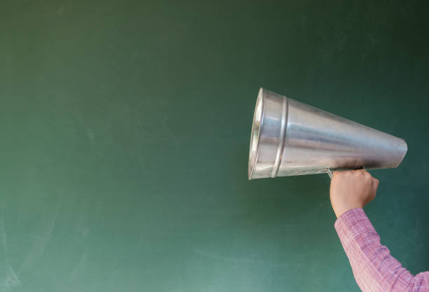 istock Hand holding a megaphone in front of a green chalkboard 1173059631