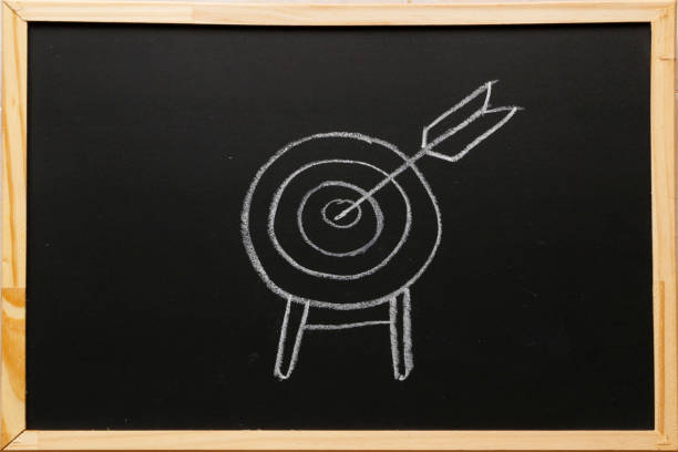 istock Write symbol on blackboard with chalk. Target with arrow, standing on a tripod. Goal achieve concept. 1173076085