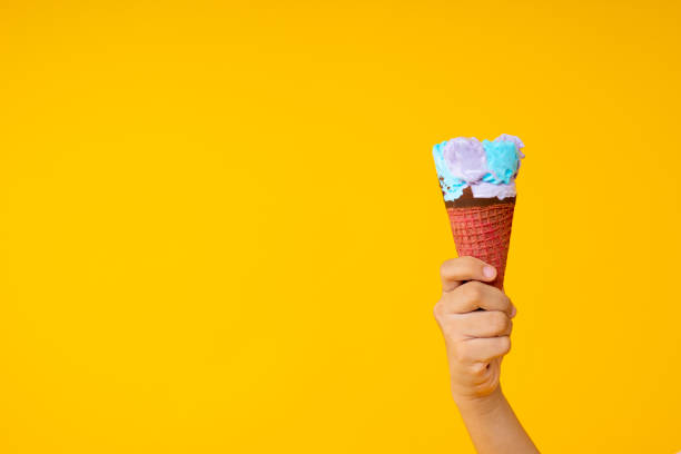 istock Close up hand holding colorful ice cream cone on yellow background with copy space 1173079920