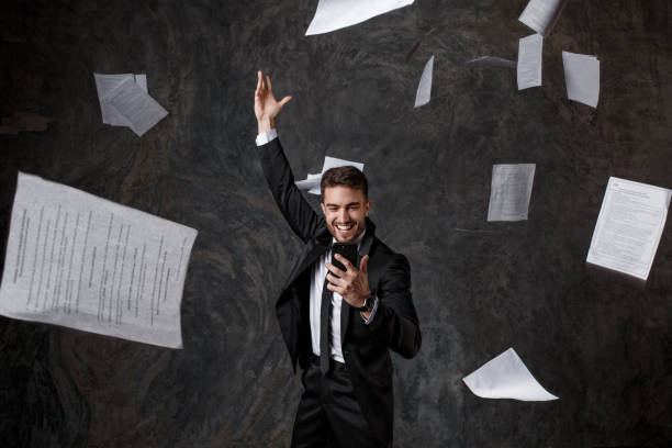 istock Concept of doing business through the phone. CRM systems and innovative technologies. failure to do business on paper. Young man throws a stack of documents looking at the phone screen 1173082377