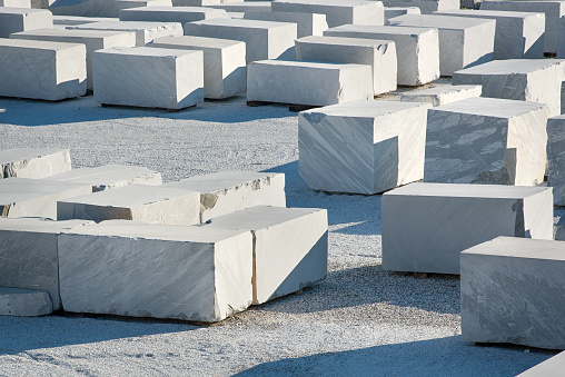 Many large rectangular blocks of white Carrara marble outdoors at a mine or quarry in Tuscany, Italy, in a concept of mining of natural resources for construction and sculpture
