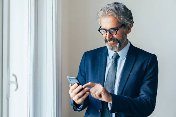 스마트 폰을 가진 사업가 - beard senior men looking away smiling 뉴스 사진 이미지