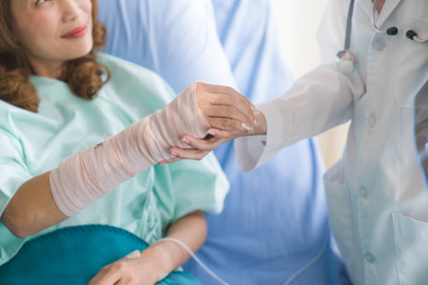 professionelle ärzte und frauen falten gebrochenen arm mit bandage der hand, während patient sitzen auf rollstuhl im krankenhaus - singapore mrt stock-fotos und bilder