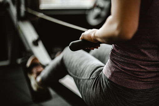 Primer plano de mujer irreconocible haciendo ejercicio en una máquina de remo en un gimnasio. photo