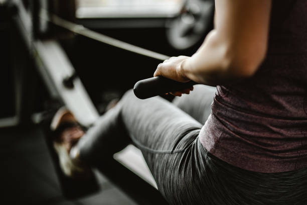 fermez-vous vers le haut de la femme méconnaissable exerçant sur la machine d'aviron dans une gymnastique. - club de remise en forme photos et images de collection