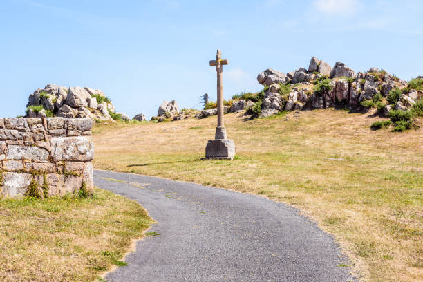 calvaire sur le côté d'une route de campagne devant un affleurement de granit un jour ensoleillé d'été en bretagne, france. - curve road in front of sign photos et images de collection