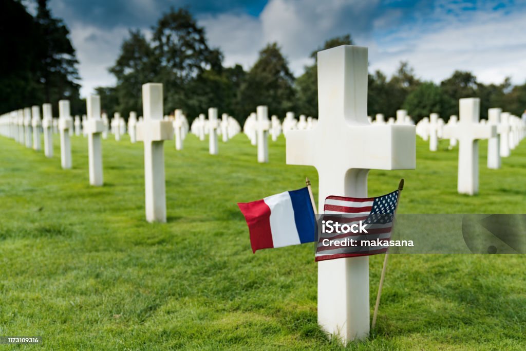 view of cross headstones in the American Cemetery at Omaha Beach in Normandy with French and US flags Selective focus view of view of cross headstones in the American Cemetery at Omaha Beach in Normandy with French and US flags Cemetery Stock Photo