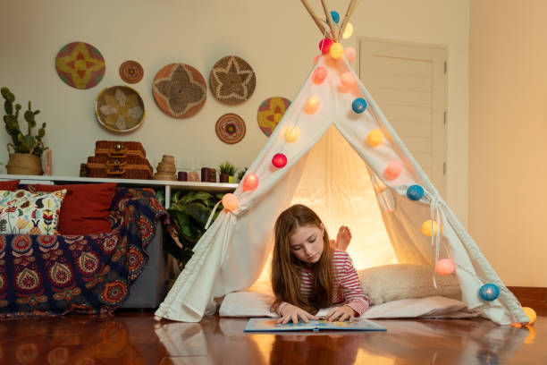 attraktive niedliche mädchen liegen und lesen buch in tipi zelt in ihrem schlafzimmer genießen glückliche zeit. - tipi bett stock-fotos und bilder