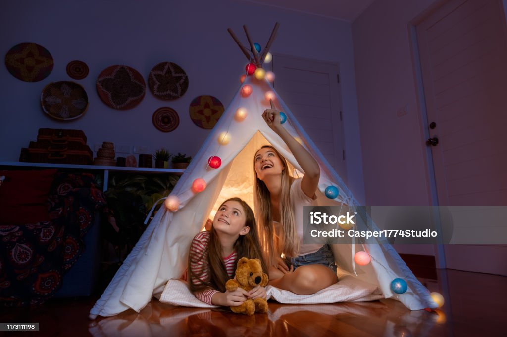 Happy mother and daughter inside tepee tent in bedroom, looking and pointing ceiling counting stars; family relationship concept. Child Stock Photo