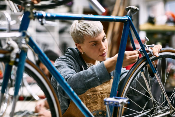 Young female employee repairing bicycle brake Young female mechanic repairing bicycle brake at workshop. Confident employee is working at repair shop. She is wearing apron. bicycle shop stock pictures, royalty-free photos & images