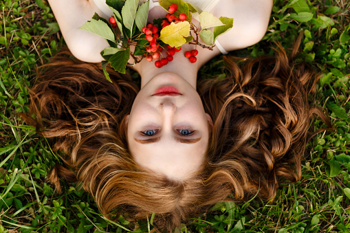 View from above top overhead of a beauty portrait of young sensual girl with red long hair lying on grass, looking at camera.