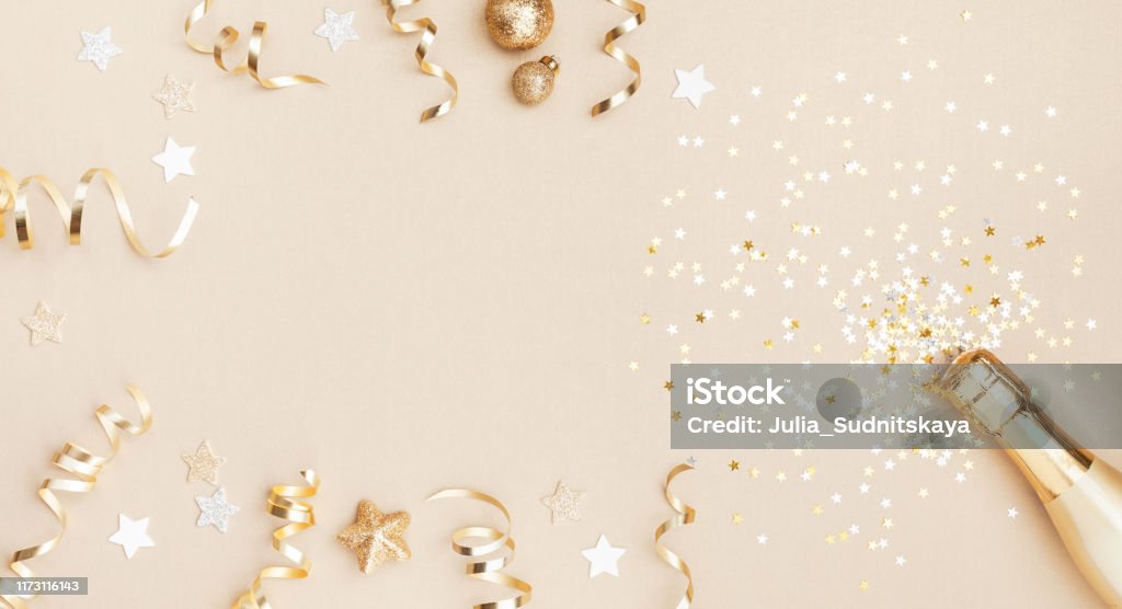 Champagne bottle with confetti stars, holiday decoration and party streamers on gold festive background. Christmas, birthday or wedding concept. Flat lay. Champagne bottle with confetti stars, holiday decoration and party streamers on gold festive background. Christmas, birthday or wedding concept. Flat lay style. Backgrounds Stock Photo