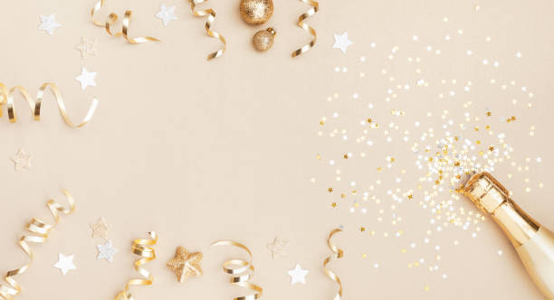 Champagne bottle with confetti stars, holiday decoration and party streamers on gold festive background. Christmas, birthday or wedding concept. Flat lay. stock photo