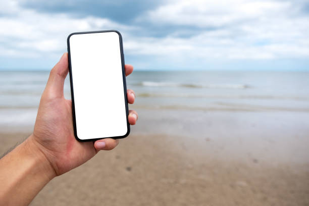 istock a hand holding and showing black mobile phone with blank desktop screen on the beach 1173116312