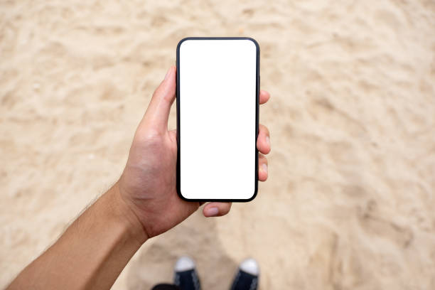 istock a man's hand holding black mobile phone with blank desktop screen while standing on the beach 1173116315