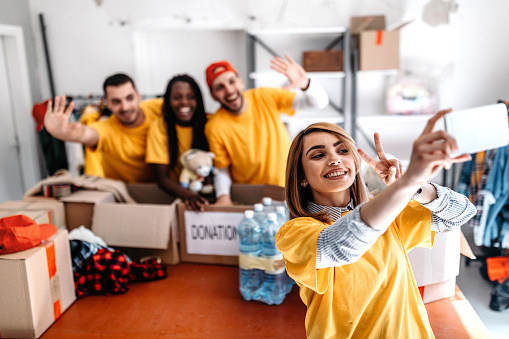 Multi-ethnic group of volunteers taking selfie while sorting donations in homeless shelter