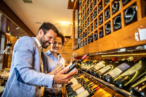 Elegant couple picking out a wine bottle for tasting from a display rack in a winery cellar.