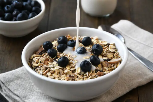 Healthy, organic homemade muesli with blueberries with almond milk pouring into bowl