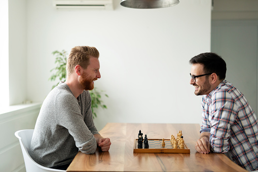 Young friends males playing chess at home