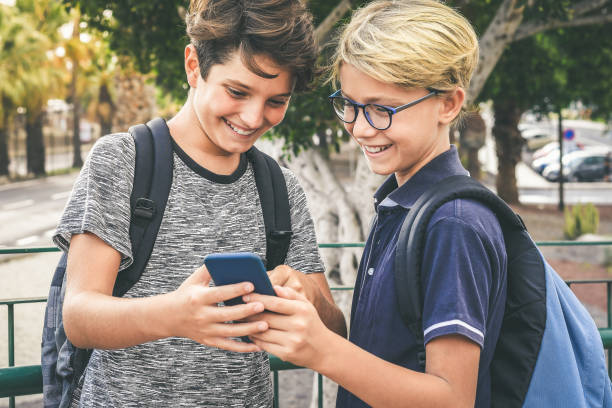 Young students smiling exciting for the first day of school. Happy boys with backpack using smartphone walking to the institute for the begin of the new school year. Youth educational concept.