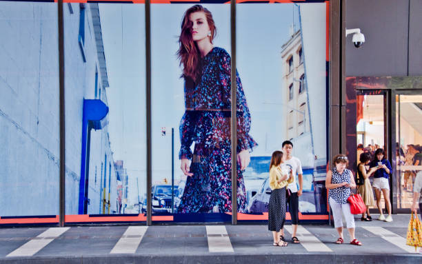 fashion high street: shoppers standing outside a clothing store displaying a huge ad board in shenzhen bay - china - market asia photography outdoors imagens e fotografias de stock