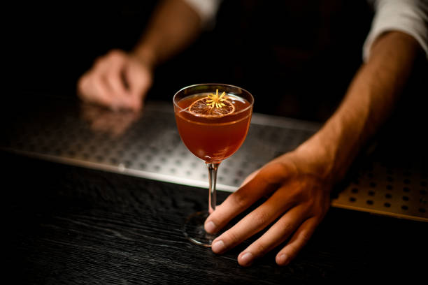 istock Bartender serving a cocktail in the glass with a caramelized lemon slice and a little yellow flower 1173132384