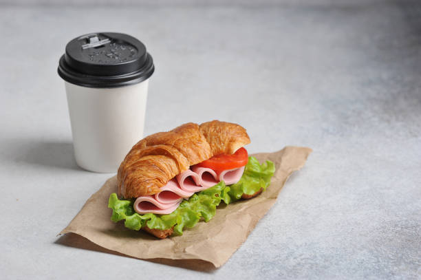 istock Coffee in a white paper cup and a ham sandwich. Coffee to go concept. 1173133778