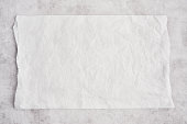 Crumpled piece of white parchment or baking paper on grey concrete background.