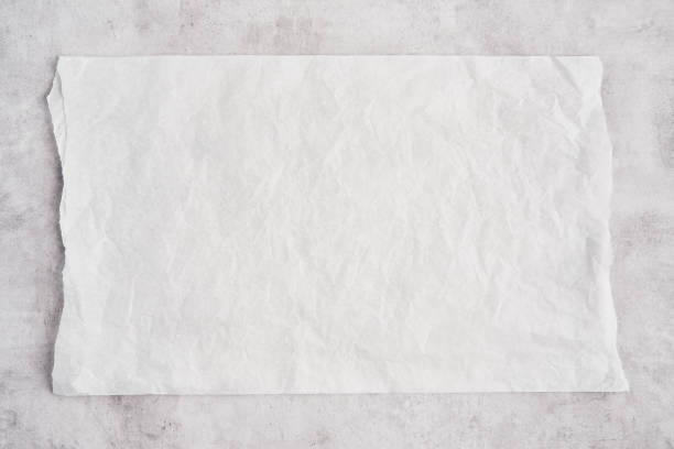 Crumpled piece of white parchment or baking paper on grey concrete background. Crumpled piece of white parchment or baking paper on grey concrete background. Top view. Copy space for text and design element. baking sheet stock pictures, royalty-free photos & images