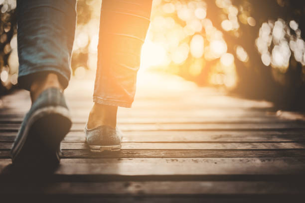 fermez-vous vers le haut de la femme marcher dedans à la nature avec le coucher du soleil et le fond de lumière du soleil. - jogging walking footpath women photos et images de collection