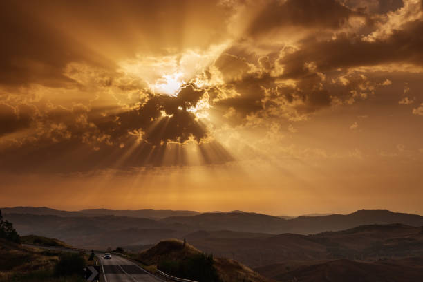 rayons de soleil se brisant à travers les nuages au coucher du soleil. ciel rouge au-dessus de colline et de montagnes.  ciel dramatique. concept de voyage. aventures de voyage en voiture. - car street horizon over land sky photos et images de collection