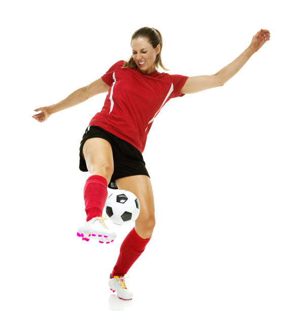 full length / front view of 20-29 years old adult beautiful brown hair / long hair caucasian female / young women soccer player / women's soccer / athlete kicking in front of white background wearing soccer uniform who is smiling / happy / cheerful - one young woman only only young women one woman only 20 25 years imagens e fotografias de stock