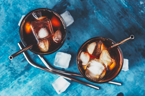 Cold brew coffee in a two glass with metal straw on a dark background. Iced coffee with ice cube. Top view.