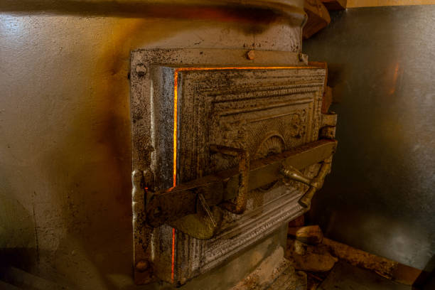 Metallic rural furnace with close doors and burning fire inside it illuminated by yellow fire light coming through it