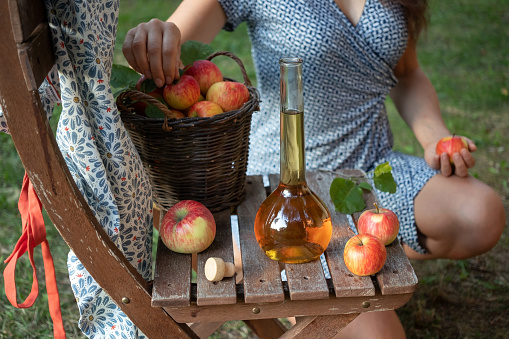 A bottle of apple cider vinegar in a garden, with a woman in the background